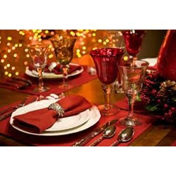 Et festligt middagsbord er dækket med røde servietter, elegante glas, sølvbestik og varme guld- og røde dekorationer med funklende lys i baggrunden.